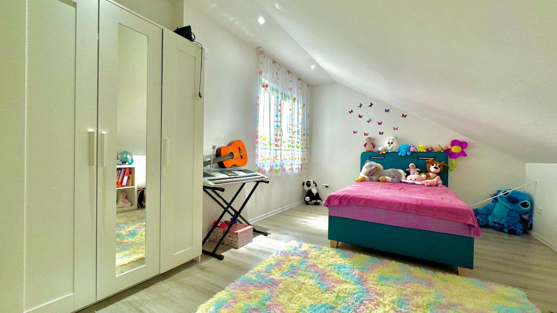 Kinderzimmer im Dachgeschoss mit farbenfrohem Teppich, weißem Kleiderschrank und Spielzeug.