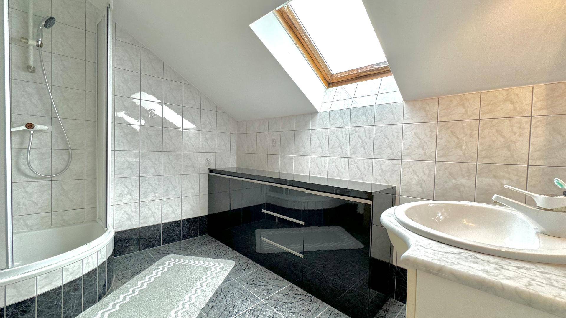 Badezimmer mit Dusche, Waschbecken und Dachfenster, gefliest in Schwarz-Weiß-Muster.