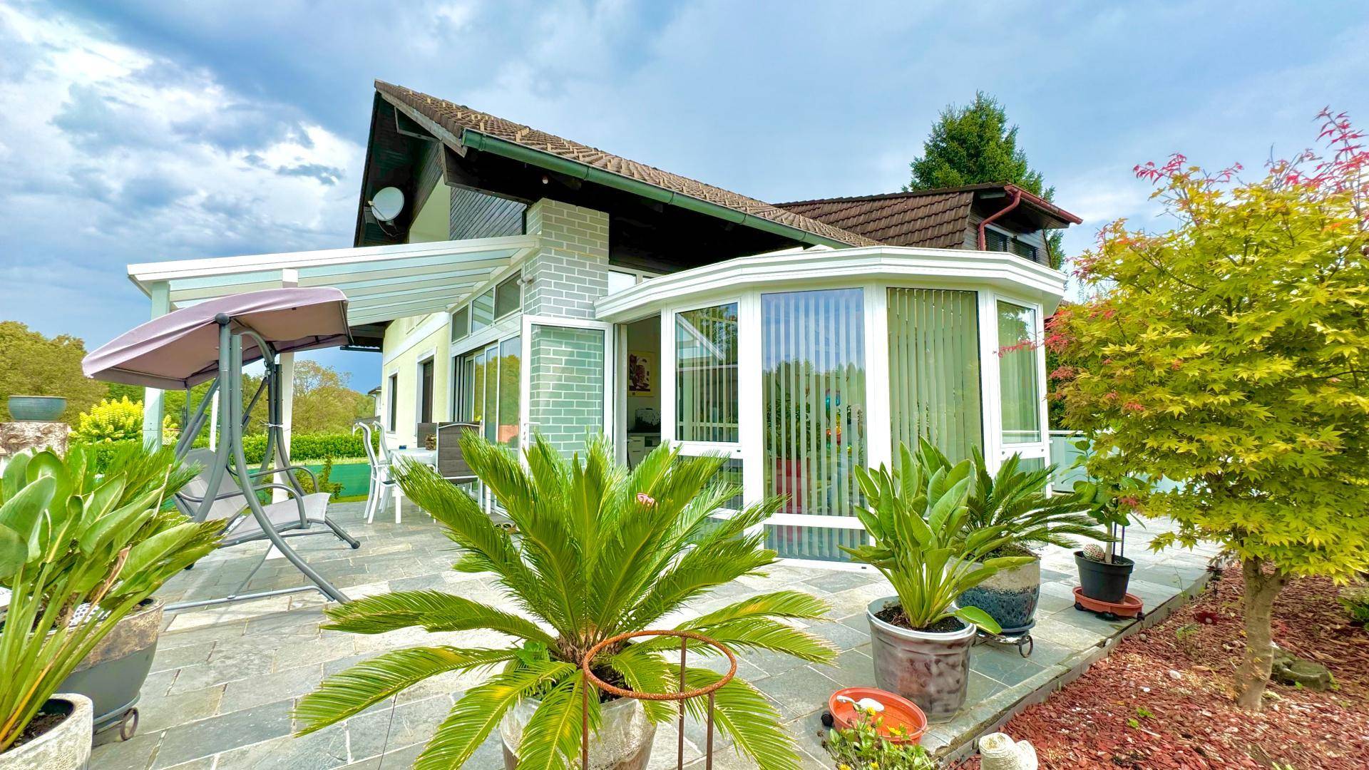 Rückansicht des Hauses mit Terrasse, Wintergarten und einem schön angelegten Garten.