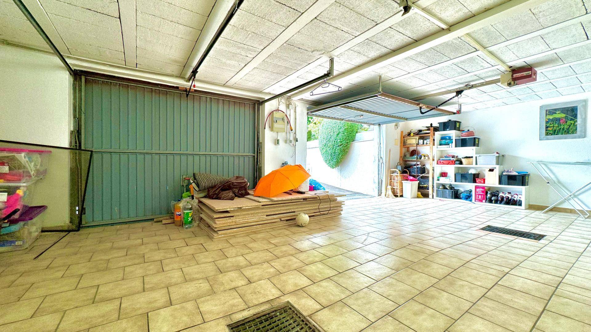 Geräumige Garage mit Fliesenboden, offenem Tor und Regalen für Lagerung.