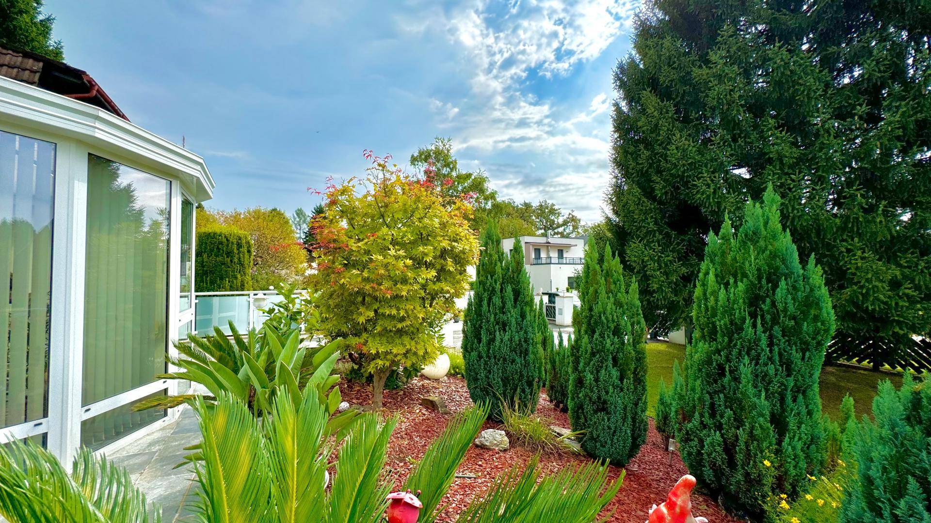 Gepflegter Gartenbereich mit vielfältigen Pflanzen und Bäumen, im Hintergrund ein weiteres Haus.