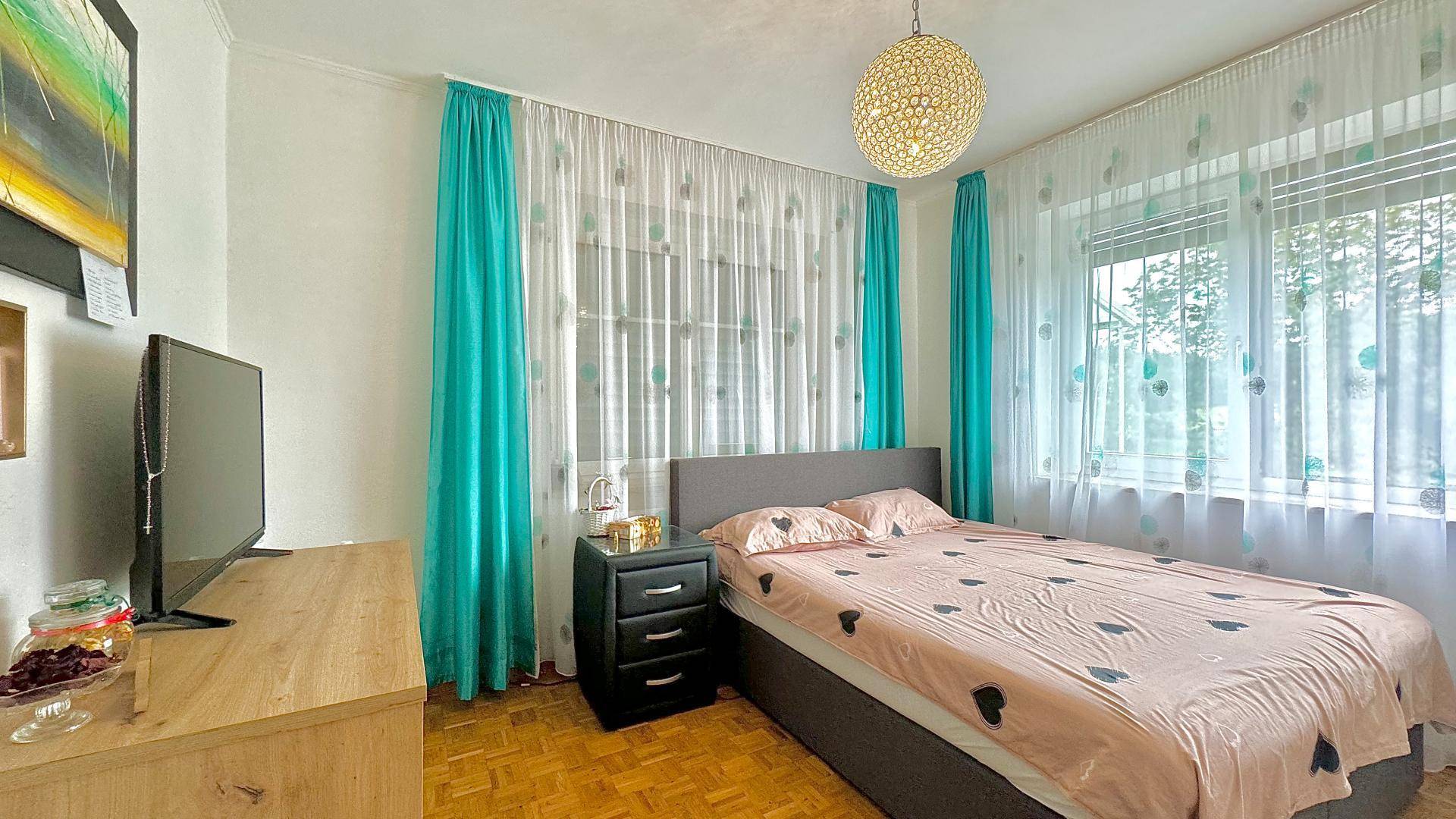 Gemütliches Schlafzimmer mit Doppelbett, Holzfußboden und farbigen Vorhängen.