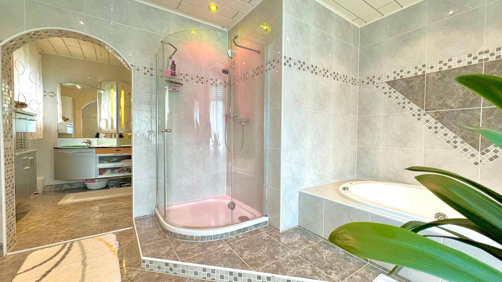 Modernes Badezimmer mit Duschkabine, Badewanne und Zugang zu einem weiteren Bereich.