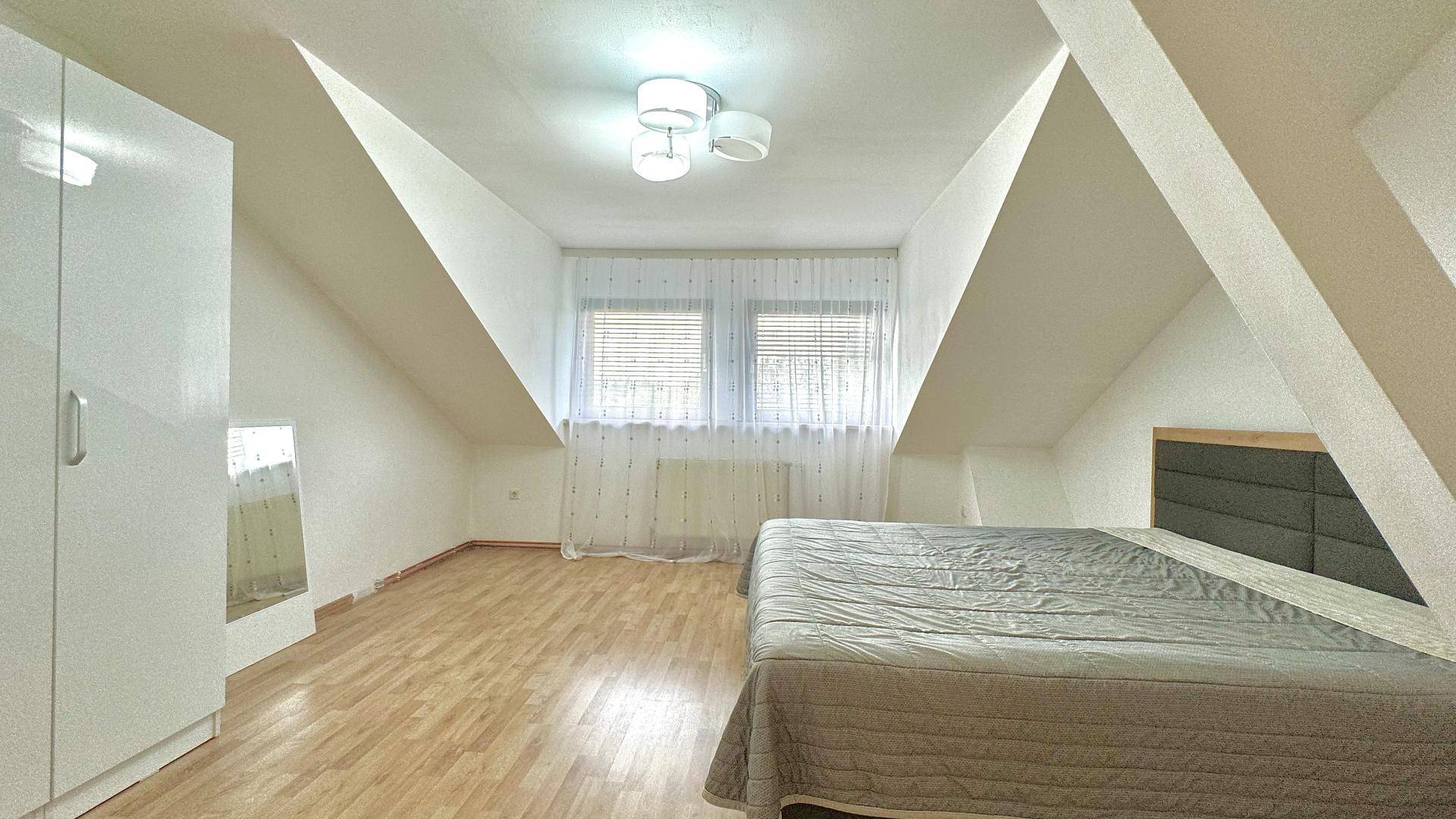 Schlafzimmer im Dachgeschoss mit Holzboden, weißem Kleiderschrank und schrägen Wänden.