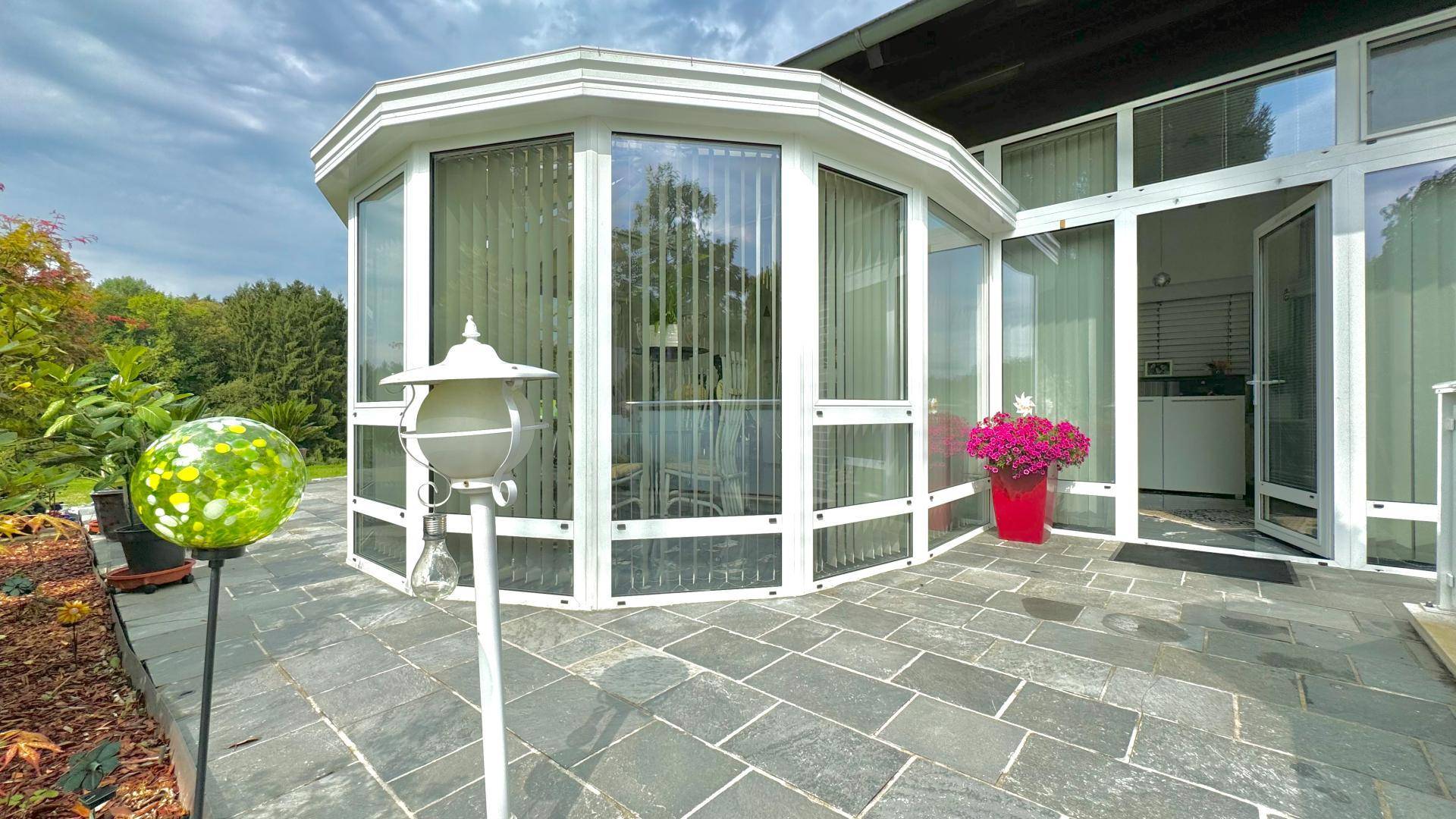 Heller Wintergarten mit Glaswänden, der auf eine gepflasterte Terrasse führt.