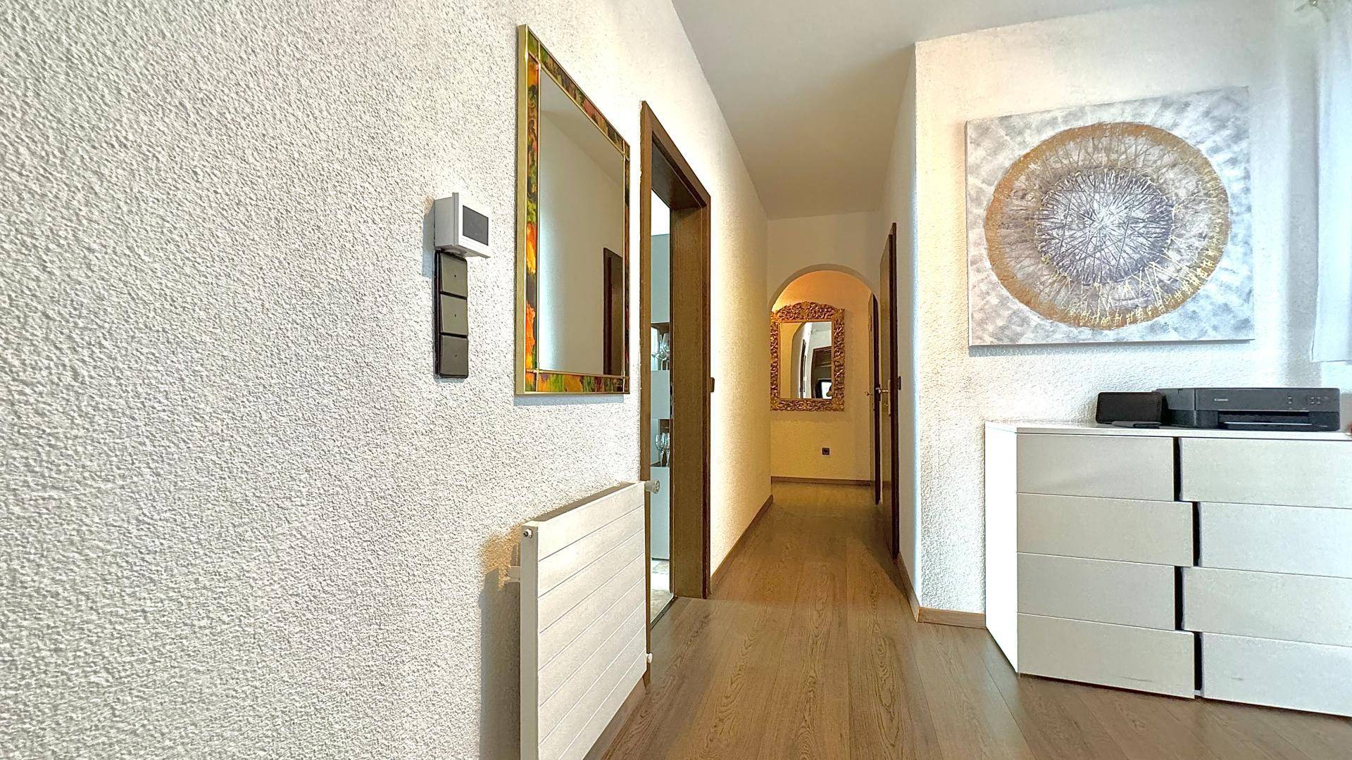 Heller Flur mit Holzfußboden, Spiegel und moderner Kommode.