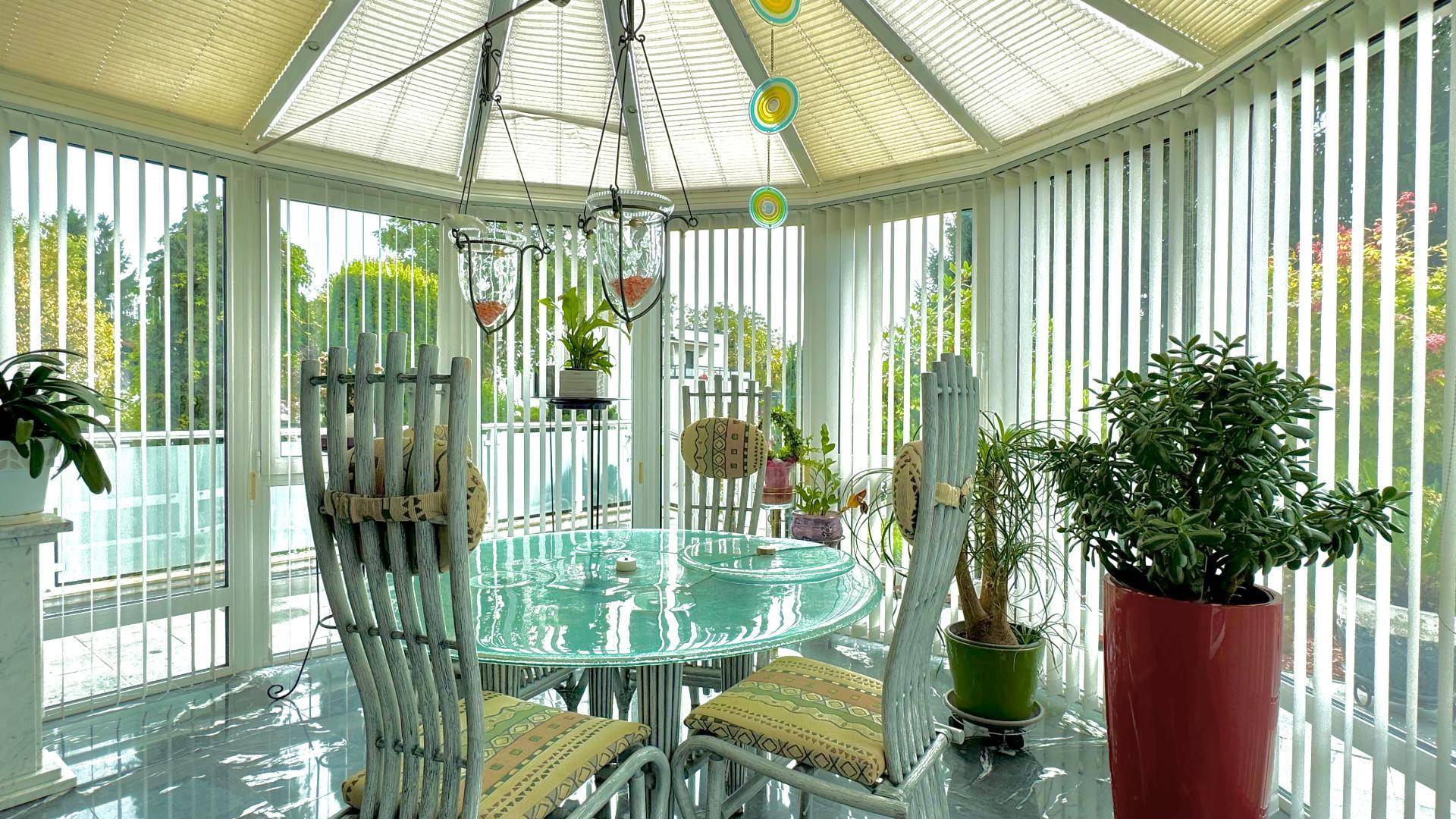 Heller Wintergarten mit Esstisch, vielen Pflanzen und weitem Blick in die Natur.