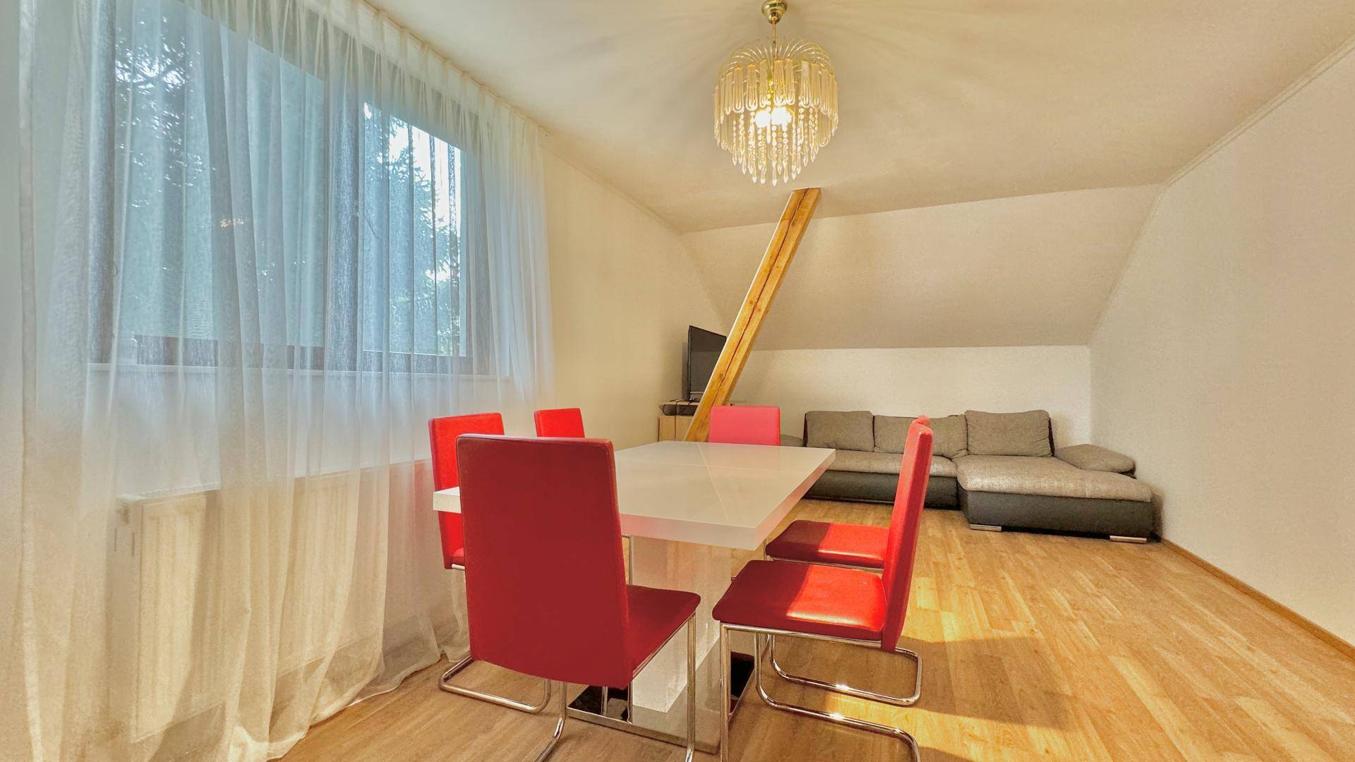 Gemütlicher Wohn- und Essbereich mit Holzboden, rotem Esstisch und Sofa unter der Dachschräge.