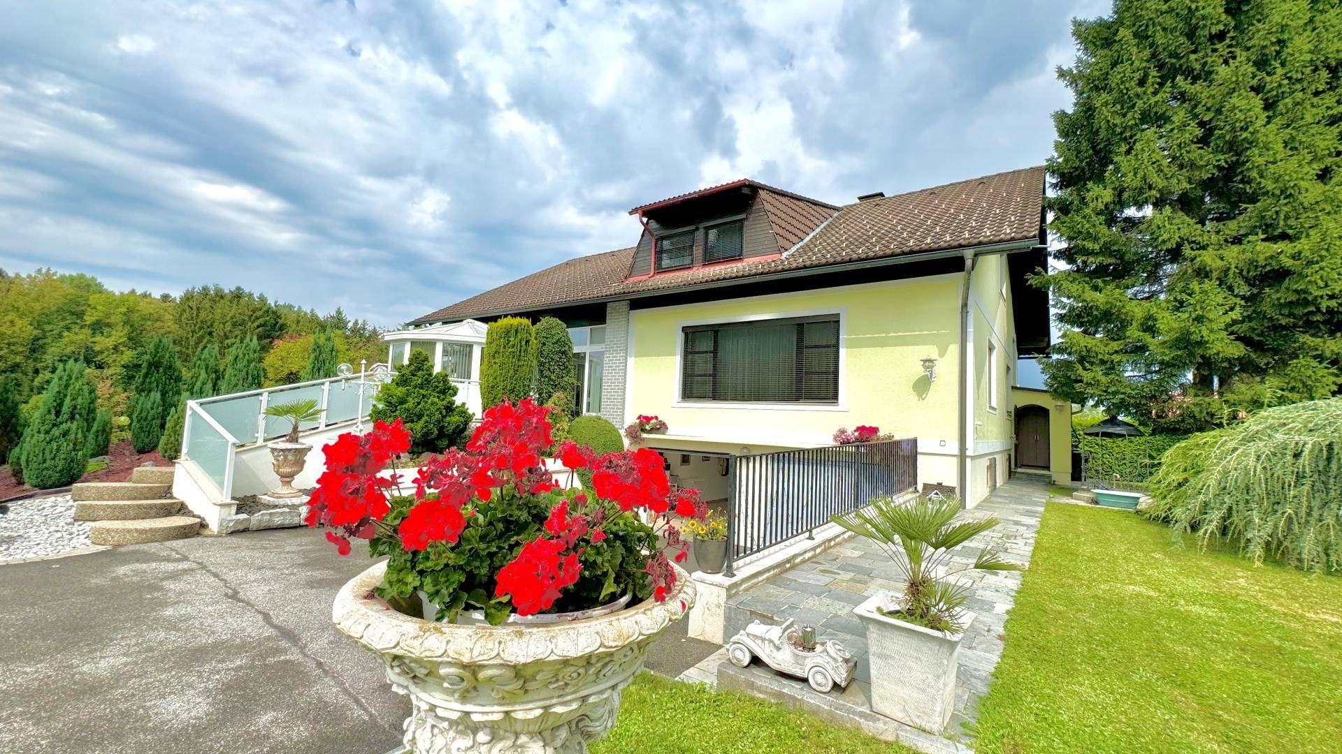 Seitenansicht des Hauses mit Zufahrt, Blumenkübeln und einem gepflegten Gartenbereich.
