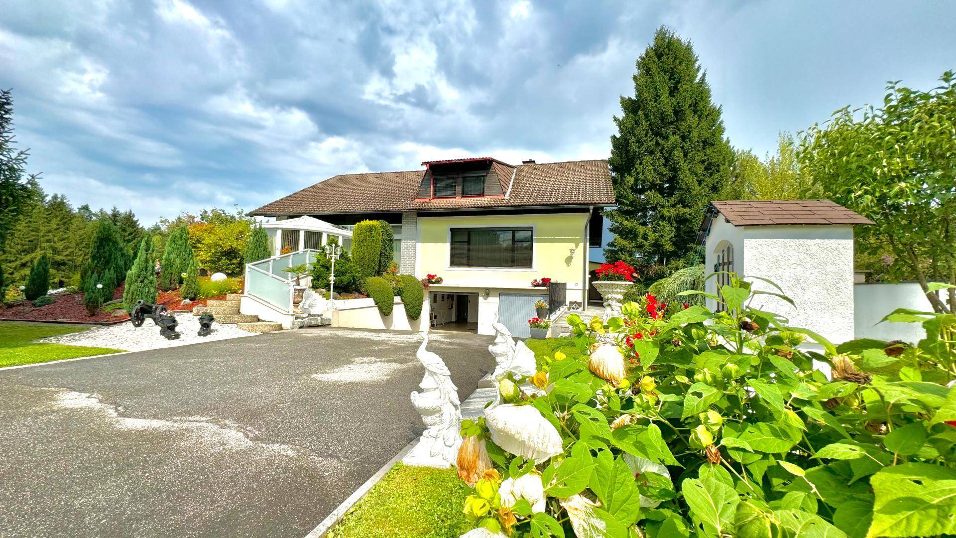Weitläufige Auffahrt zum Haus mit hellgrüner Fassade, umgeben von Bäumen und dekorativen Elementen.