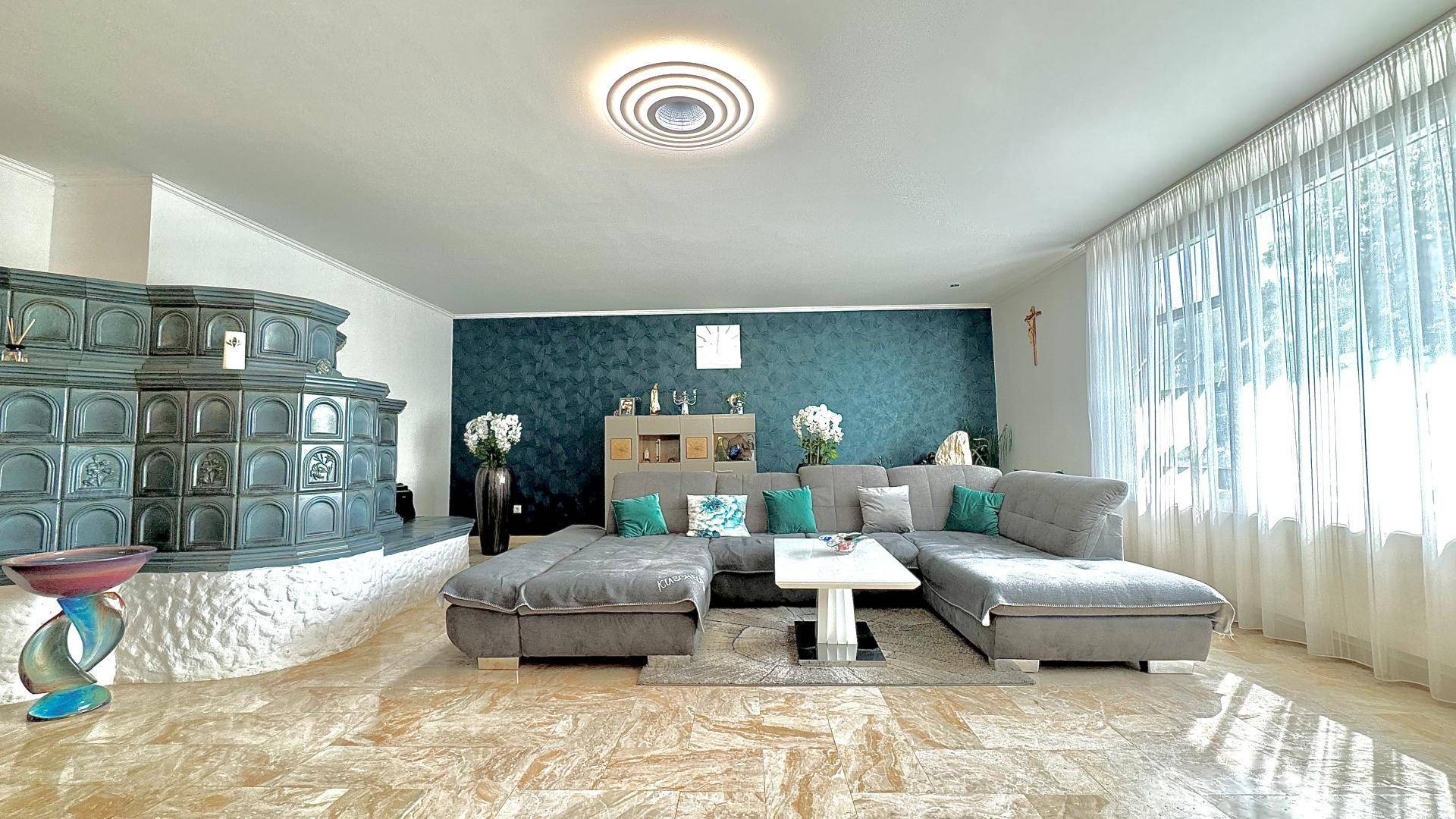Geräumiges Wohnzimmer mit großem Ecksofa, Kachelofen und gemustertem Fliesenboden.