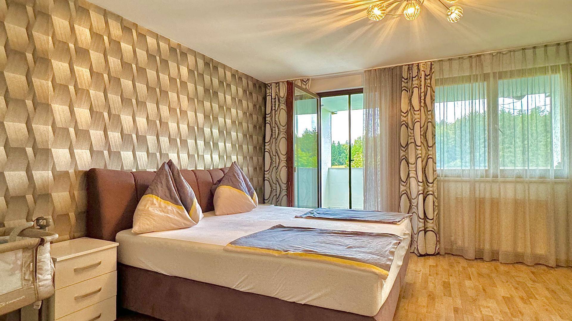 Schlafzimmer mit gemusterter Tapete, Doppelbett und direktem Zugang zu einem Balkon.