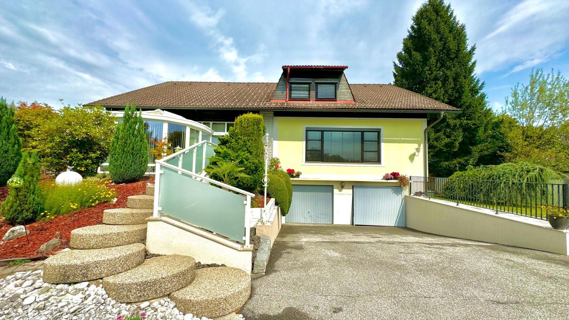 Vorderansicht des Hauses mit gelber Fassade, Garagentoren und gepflegtem Vorgarten.