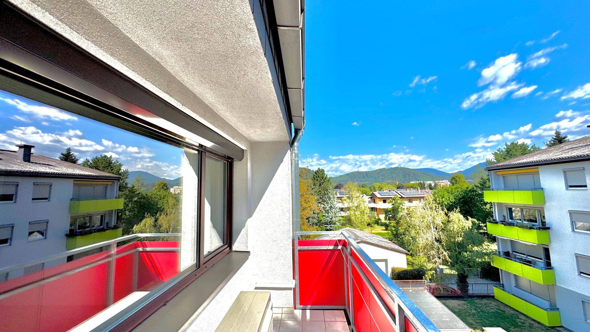 Balkon mit rotem Geländer und weitem Blick auf die umliegende Wohngegend und Berge.