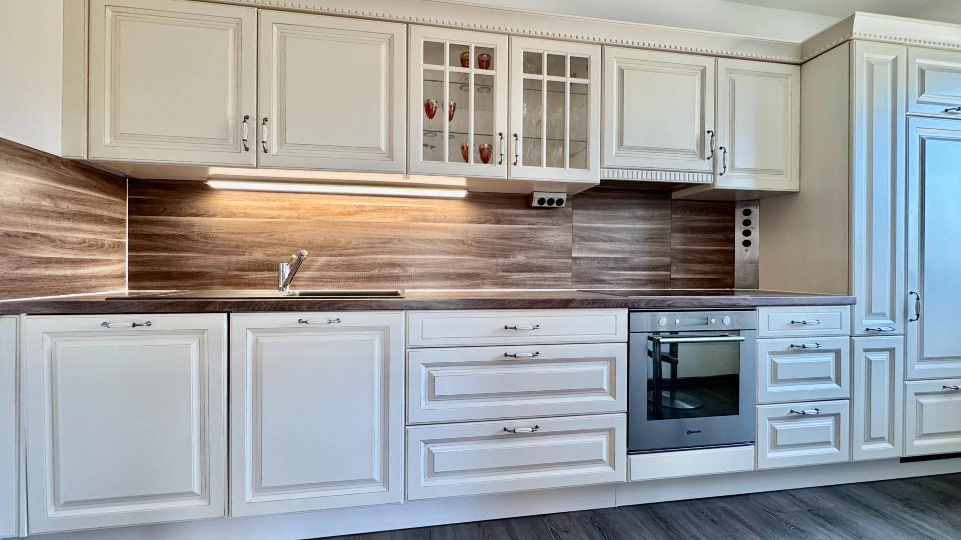 Detailansicht der Küche mit weißen Schränken, Holzoptik-Arbeitsplatte und integriertem Backofen.
