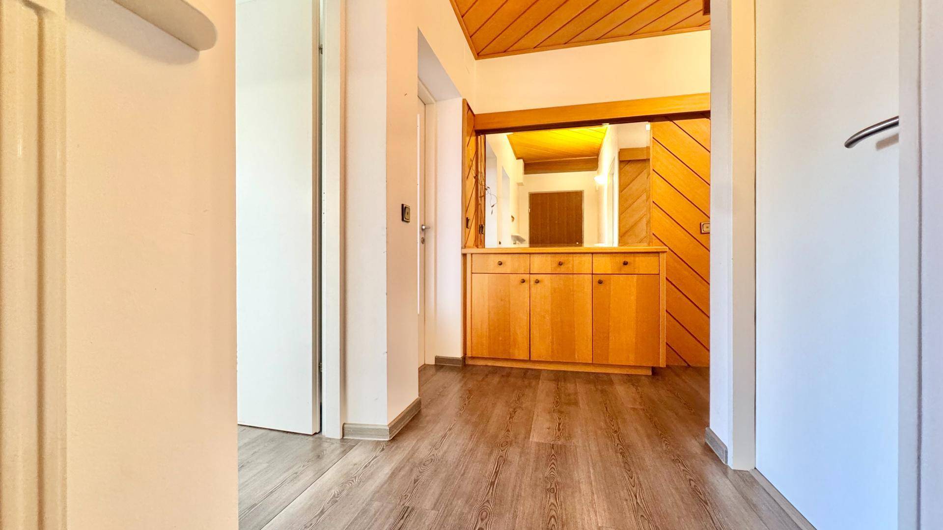 Flur mit Holzvertäfelung, Einbauschrank und Spiegel, sowie dunklem Laminatboden.