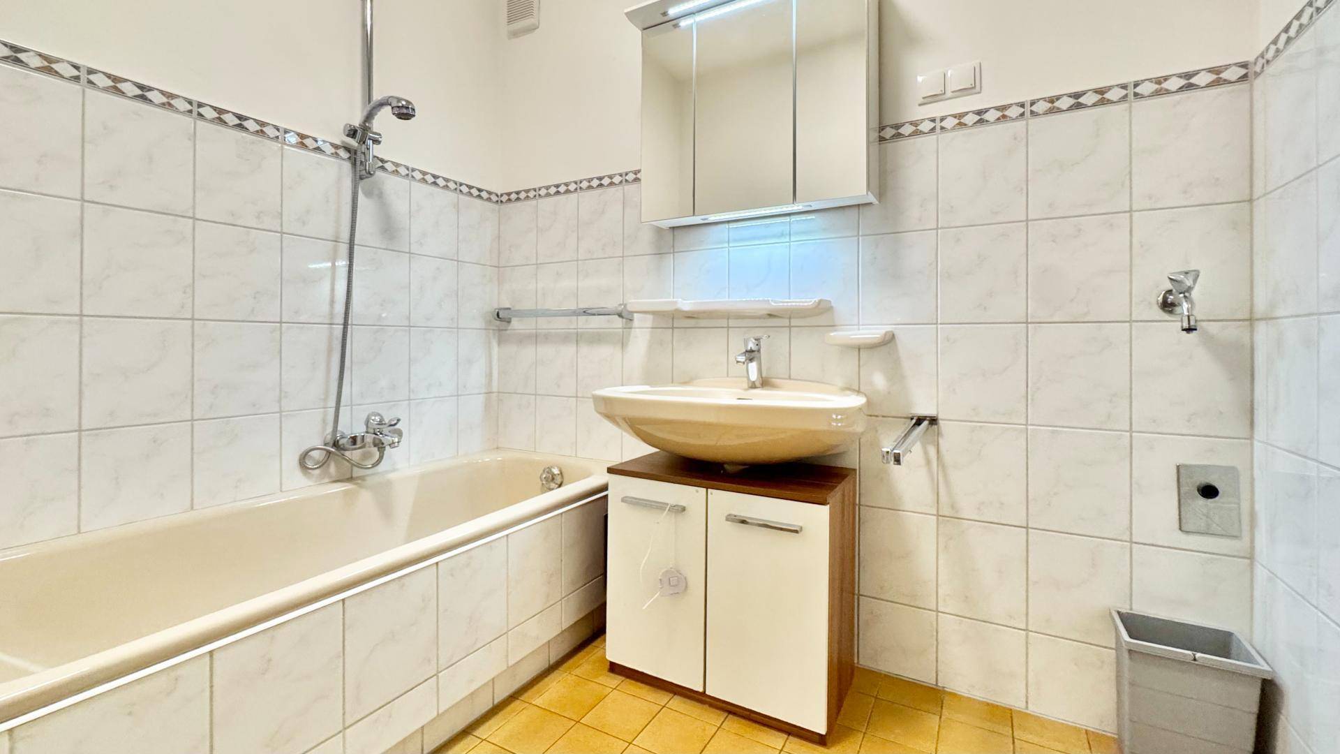 Badezimmer mit Badewanne, Waschbecken und Spiegelschrank, gefliest in hellen Tönen.