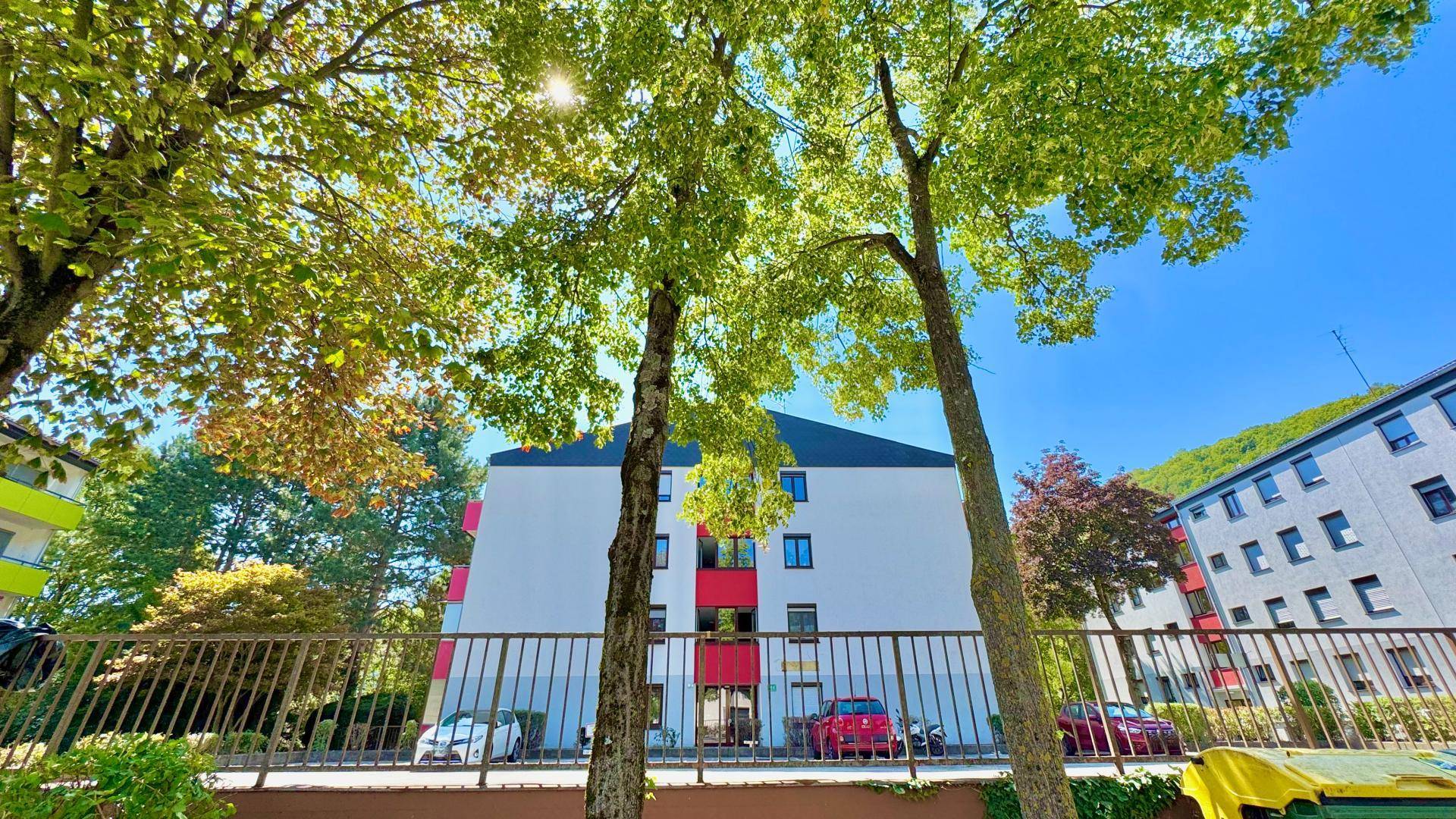Mehrfamilienhaus mit grünen Bäumen im Vordergrund und blauer Himmel.