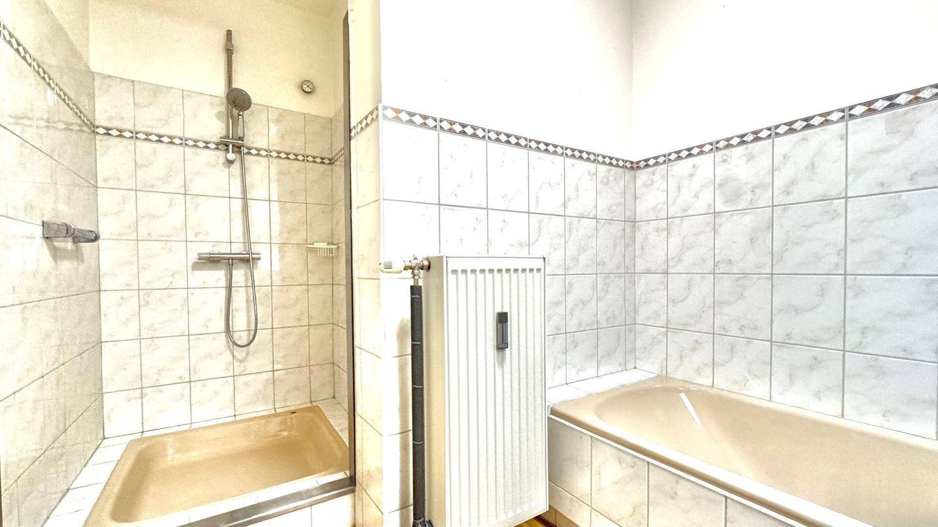 Badezimmer mit Badewanne und separater Dusche, gefliest in hellen Tönen.