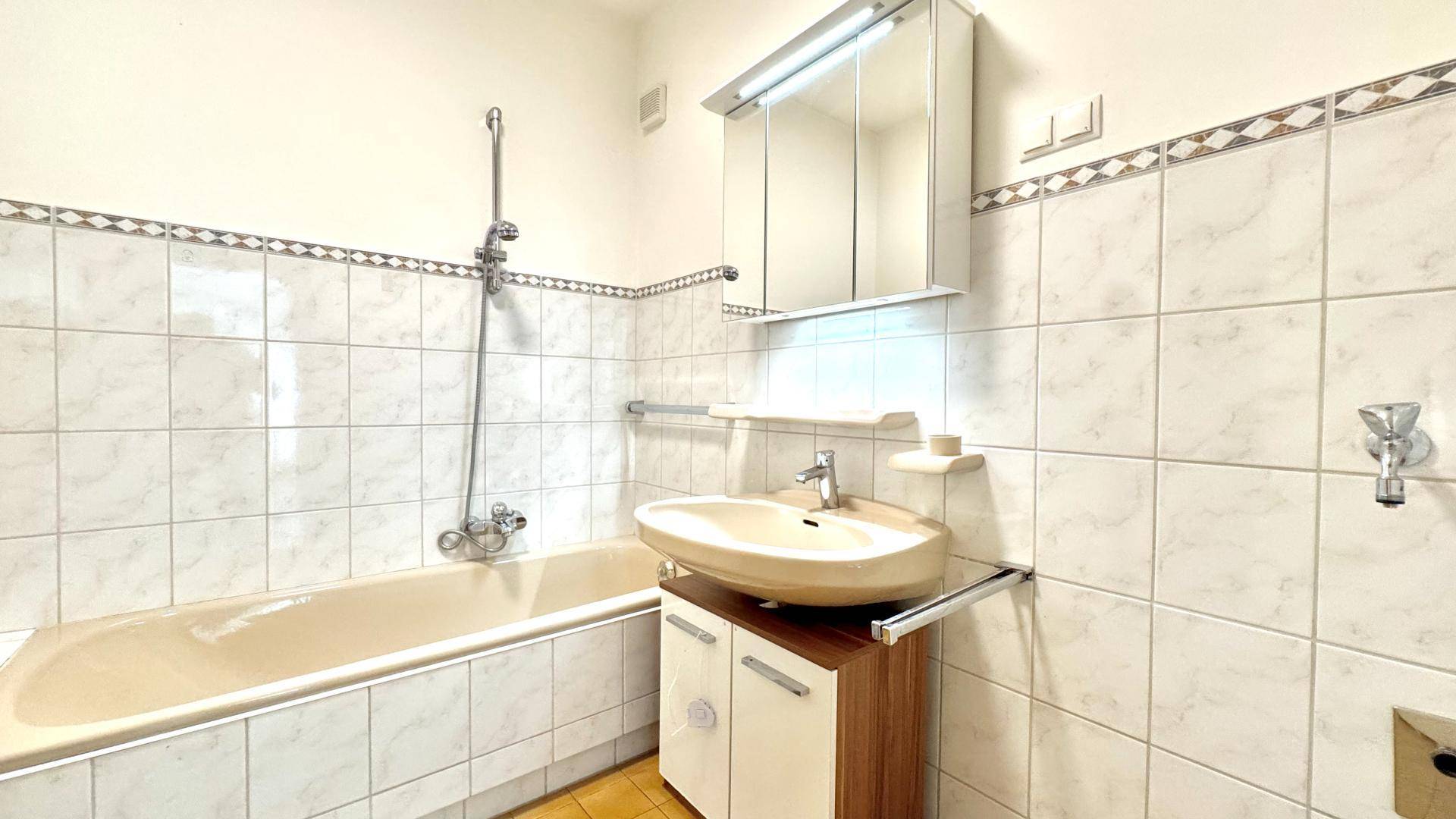 Badezimmer mit Badewanne, Waschbecken und Spiegelschrank, gefliest in hellen Tönen.