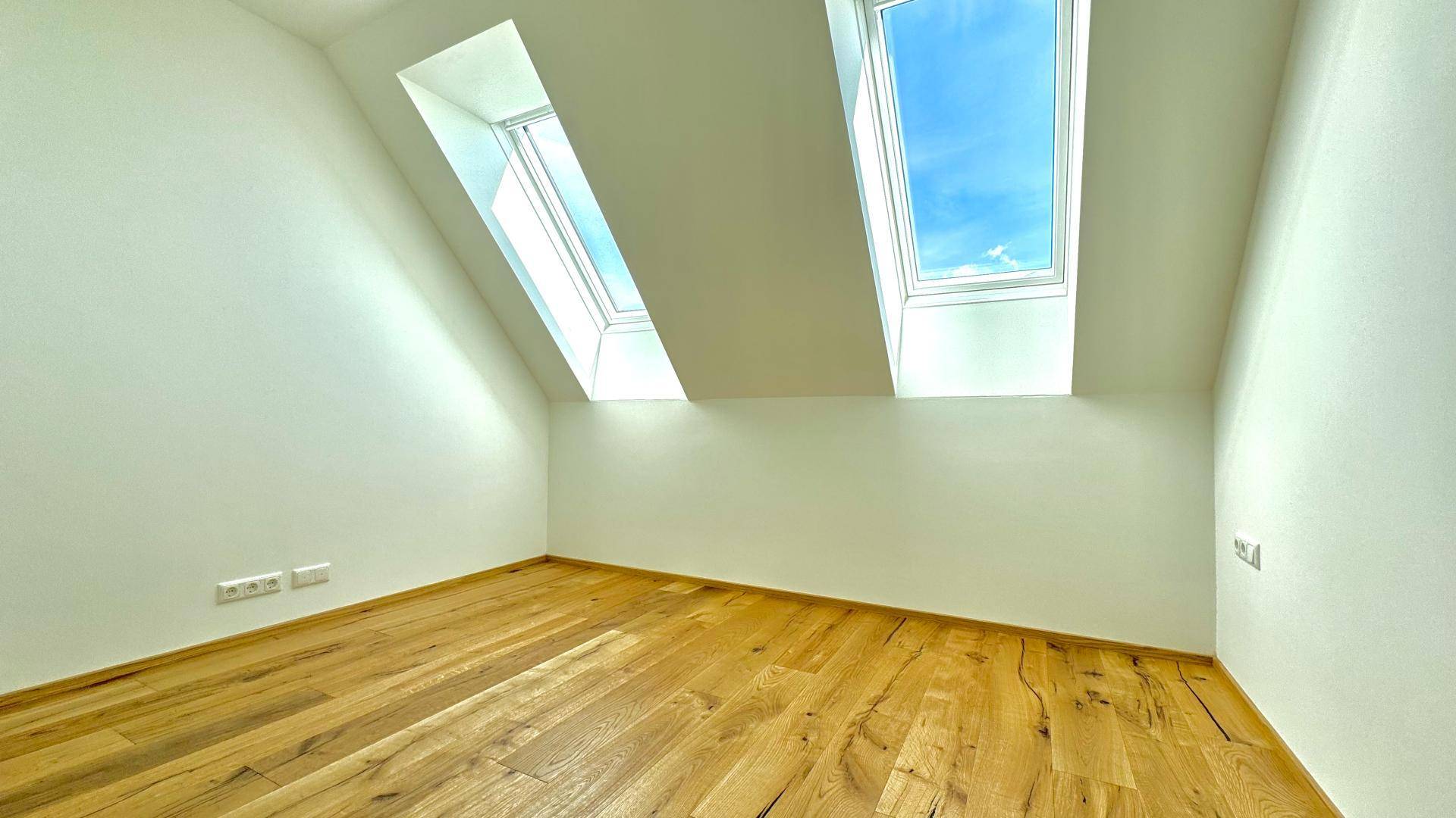 Helles Dachzimmer mit zwei Oberlichtern, Holzboden und schrägen Wänden für viel Tageslicht.