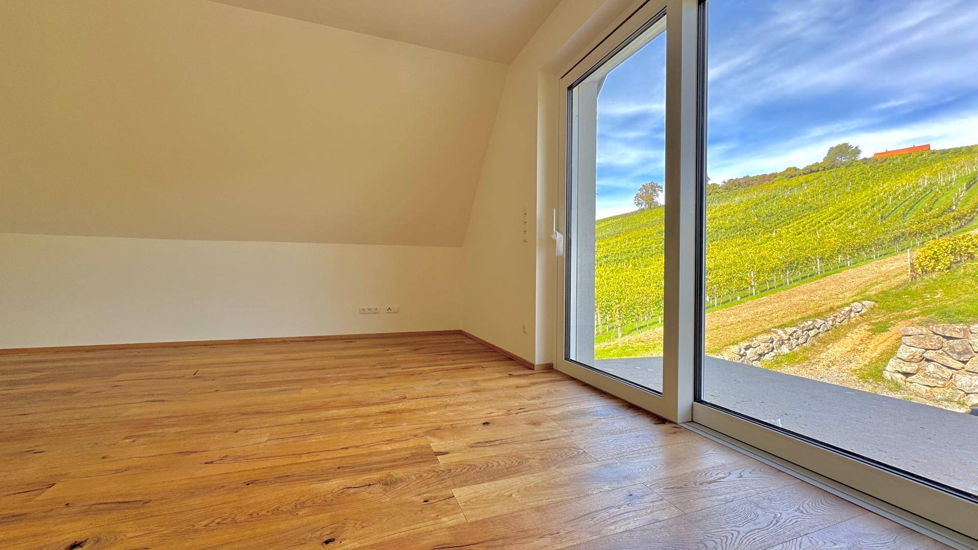 Geräumiges Zimmer im Dachgeschoss mit Holzboden und großer Schiebetür mit Blick auf die Weinberge.