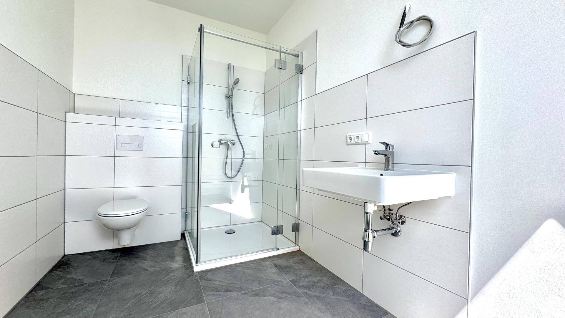 Modernes Badezimmer mit ebenerdiger Dusche, wandhängendem WC und Einzelwaschbecken.
