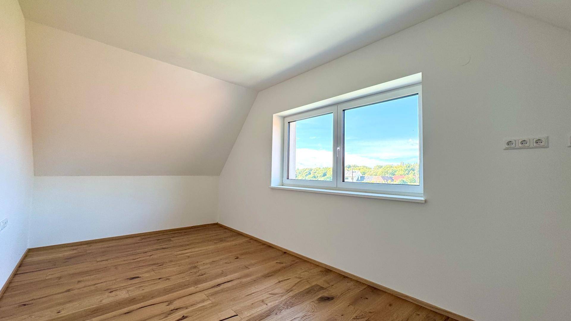 Gemütliches Dachzimmer mit Holzboden und Fenster, das einen weiten Blick in die Ferne ermöglicht.