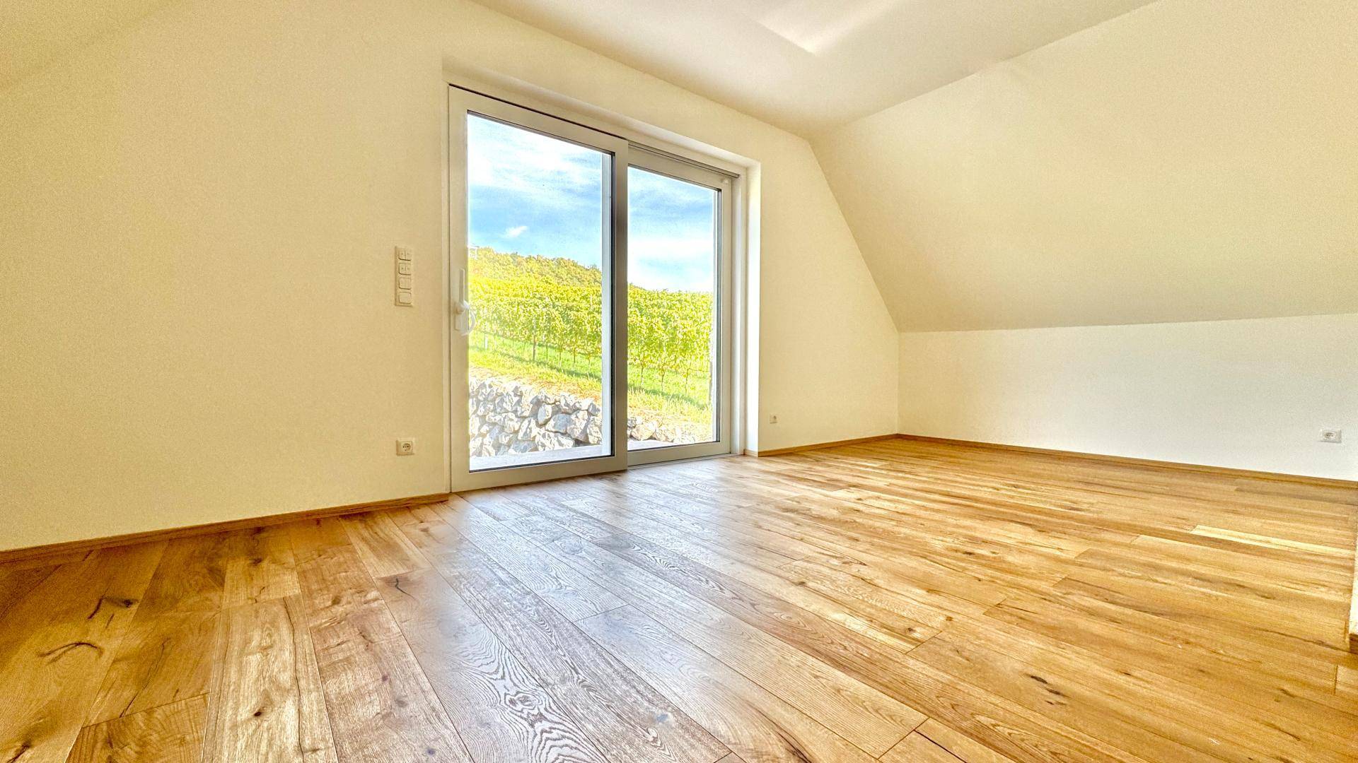 Helles Dachzimmer mit warmem Holzboden und weitem Ausblick auf die umliegenden Weinberge.