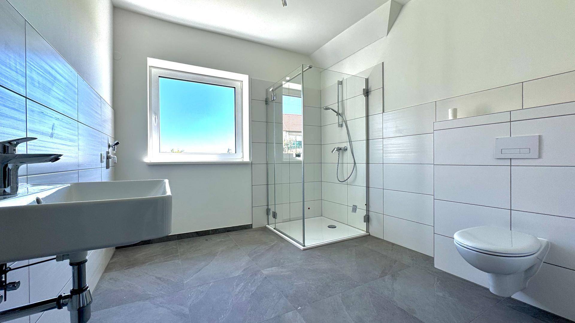 Helles Badezimmer mit weißen und blauen Fliesen, moderner Dusche und wandhängender Toilette.