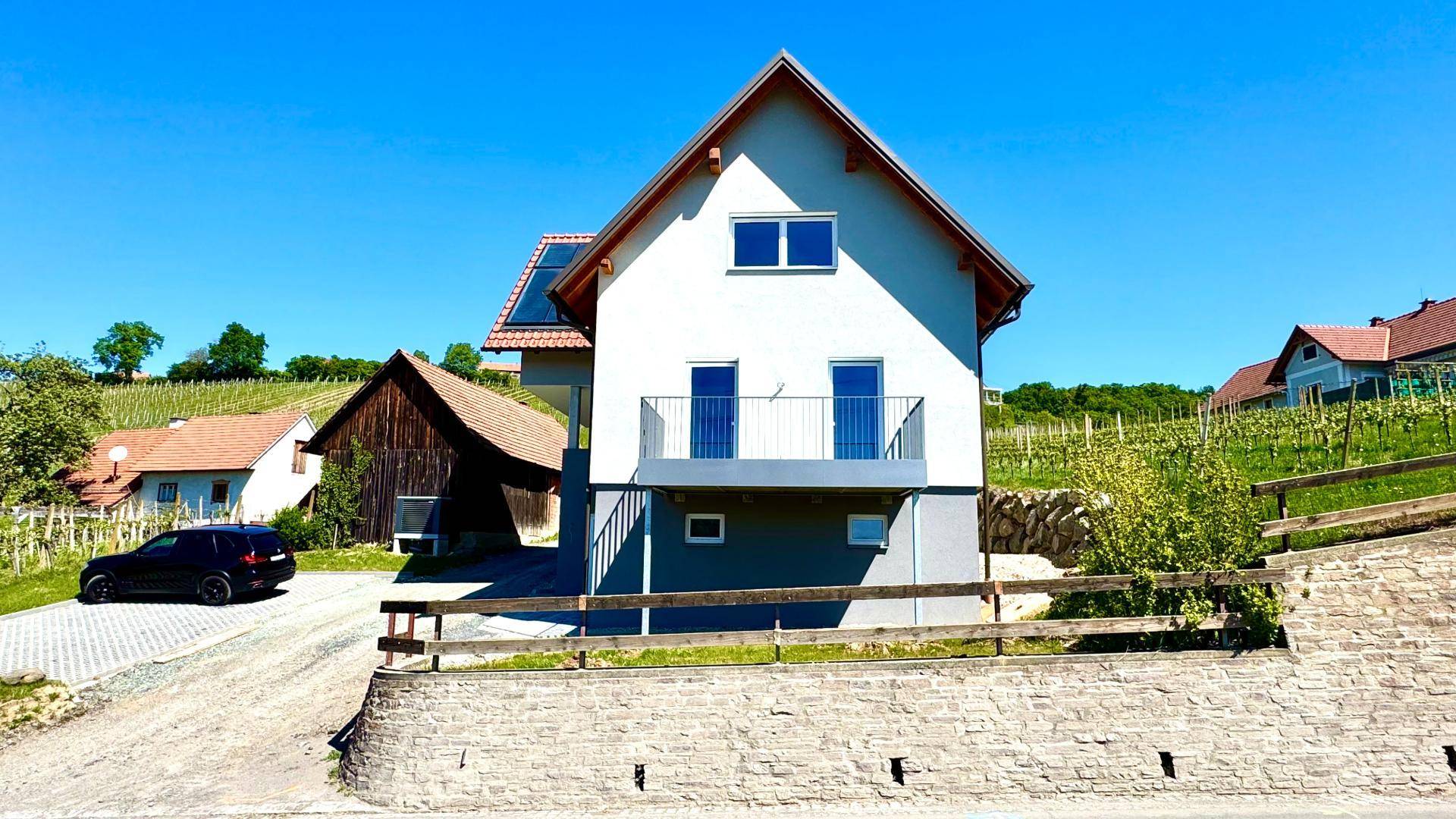 Vorderansicht des Neubaus mit Balkon, rotem Dach und der malerischen Weinlandschaft.