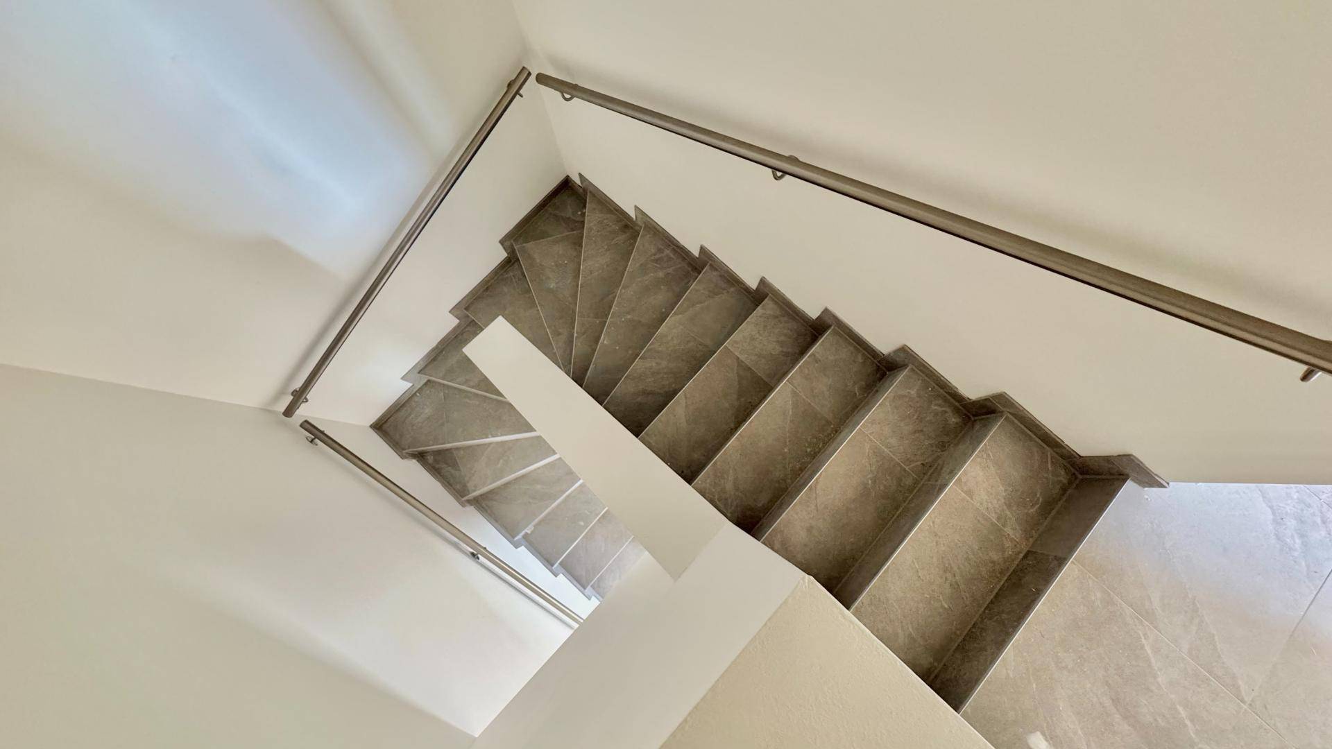 Blick von oben auf eine moderne Treppe mit grauen Fliesen und eleganten Handläufen.