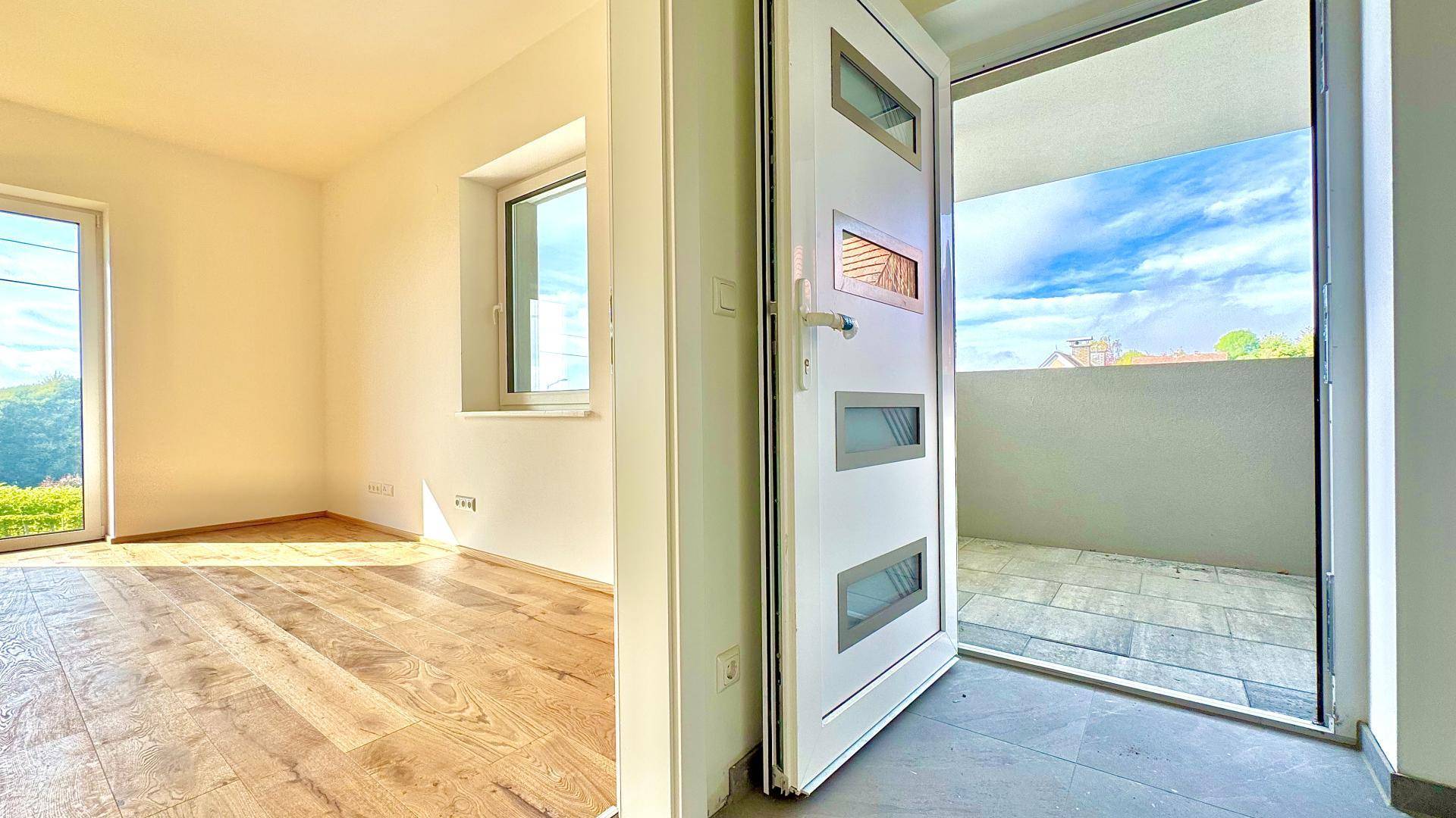 Heller Eingangsbereich mit Zugang zu einem kleinen Balkon und Blick in ein weiteres Zimmer.