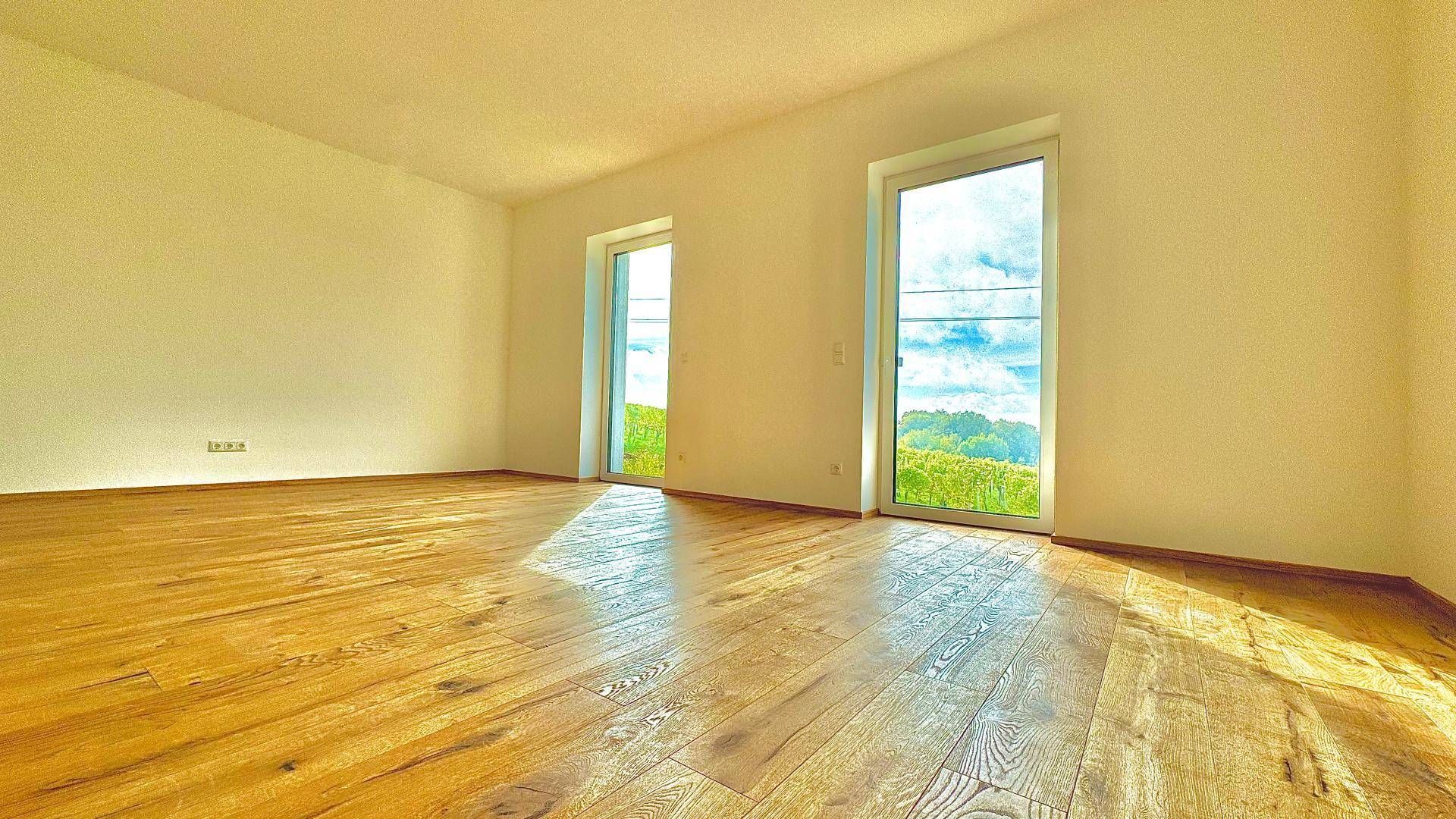 Geräumiges Zimmer mit hellem Holzboden und zwei großen Fenstern mit Blick auf die umliegenden Weinberge.