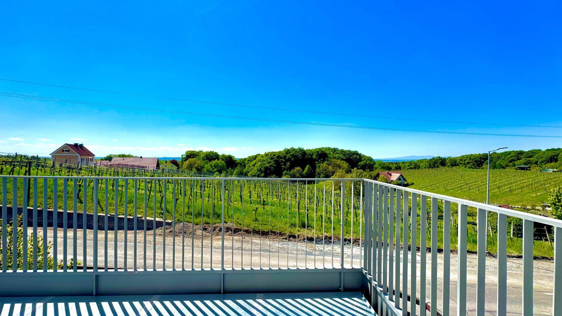 Heller Balkon mit modernem Geländer und weitem Blick über Weinberge bis zum Horizont.
