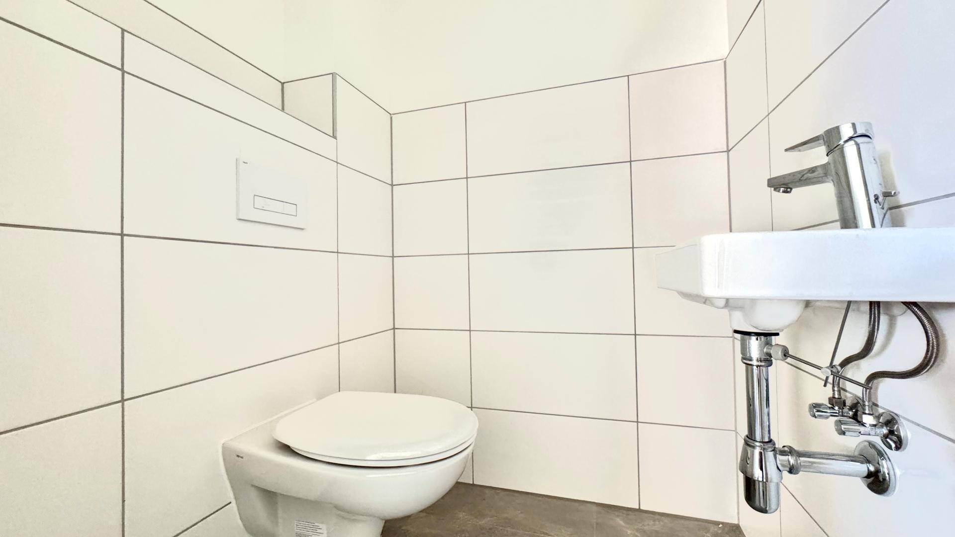 Kleines, hell gefliestes Gäste-WC mit wandhängender Toilette und modernem Waschbecken.