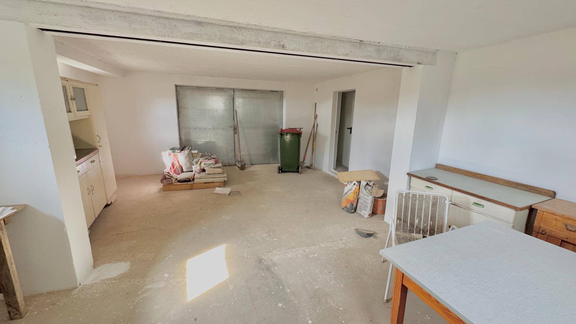Großer, unfertiger Mehrzweckraum mit Betonboden und einer breiten Metalltür im Hintergrund.