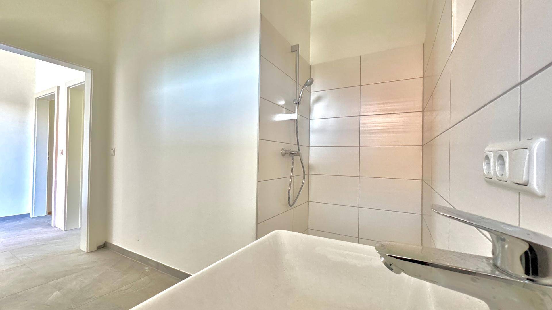 Modernes Badezimmer mit weißen Fliesen, Duschbereich und einem Waschbecken.