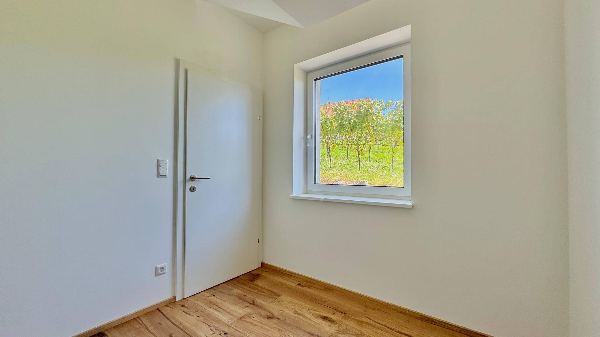 Heller Raum mit Holzboden und einem Fenster, das einen schönen Blick auf die Weinreben bietet.