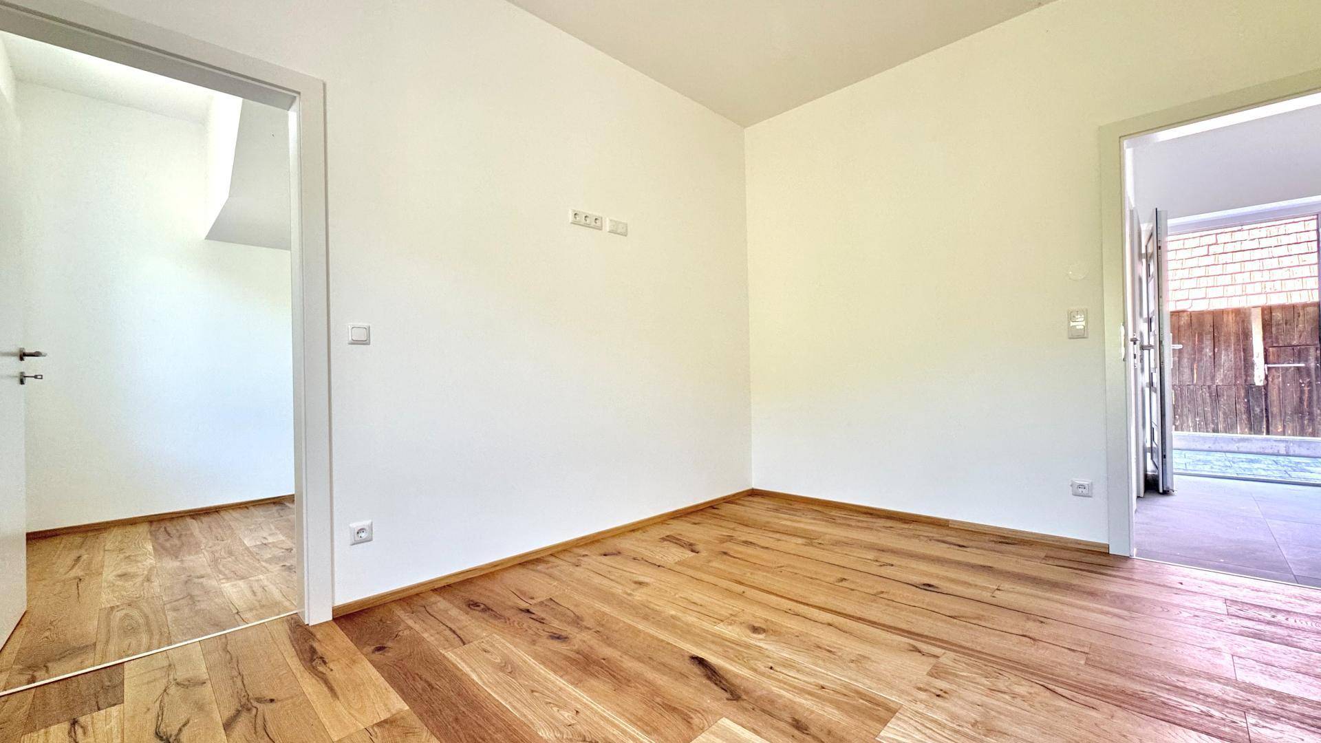 Leerer Raum mit Holzboden und offenem Zugang zu einem Außenbereich mit Holzzaun.