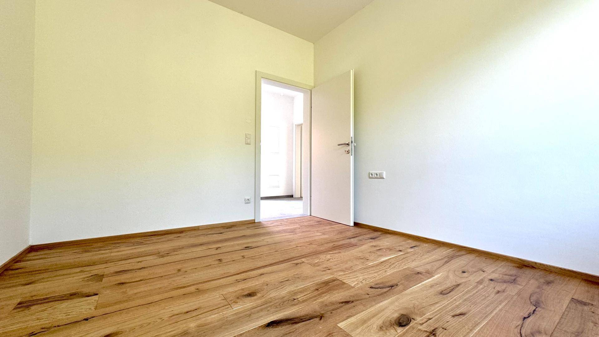 Leerer Raum mit Holzboden und offener Tür, die zu einem weiteren Zimmer führt.
