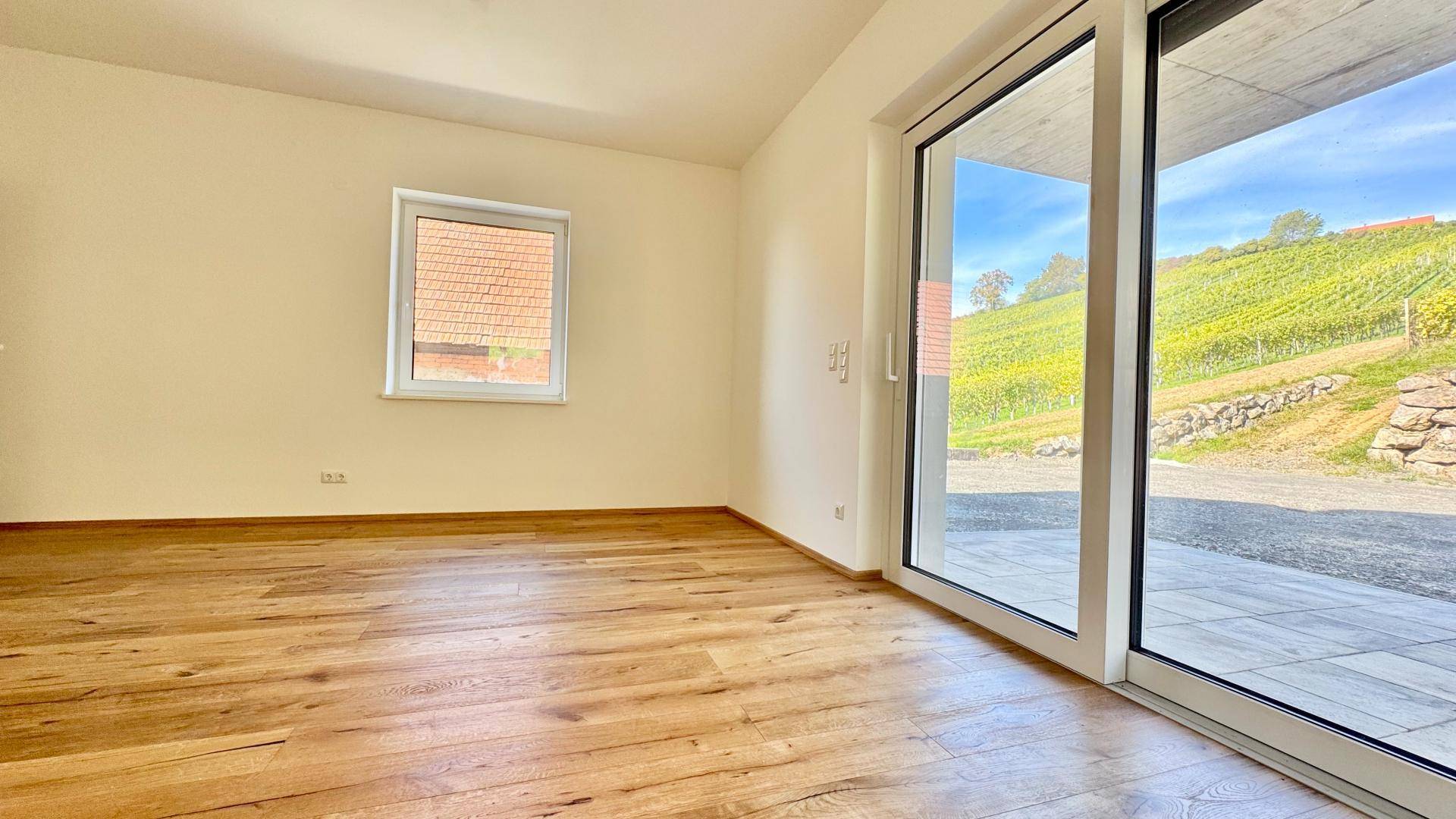 Geräumiger, heller Raum mit Holzboden und direktem Zugang zur Terrasse mit Weinbergpanorama.