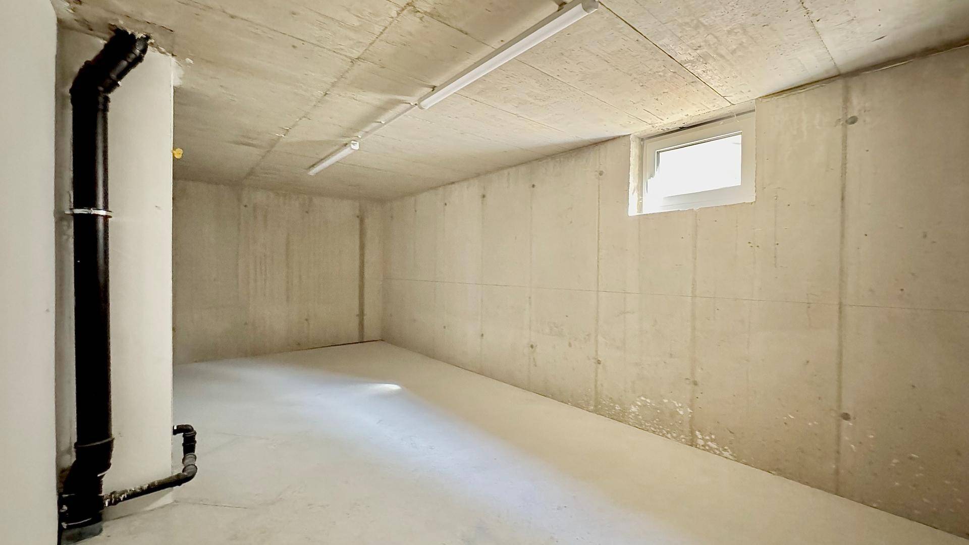 Unausgebauter Kellerraum mit Betonwänden und -boden sowie einem kleinen Fenster.