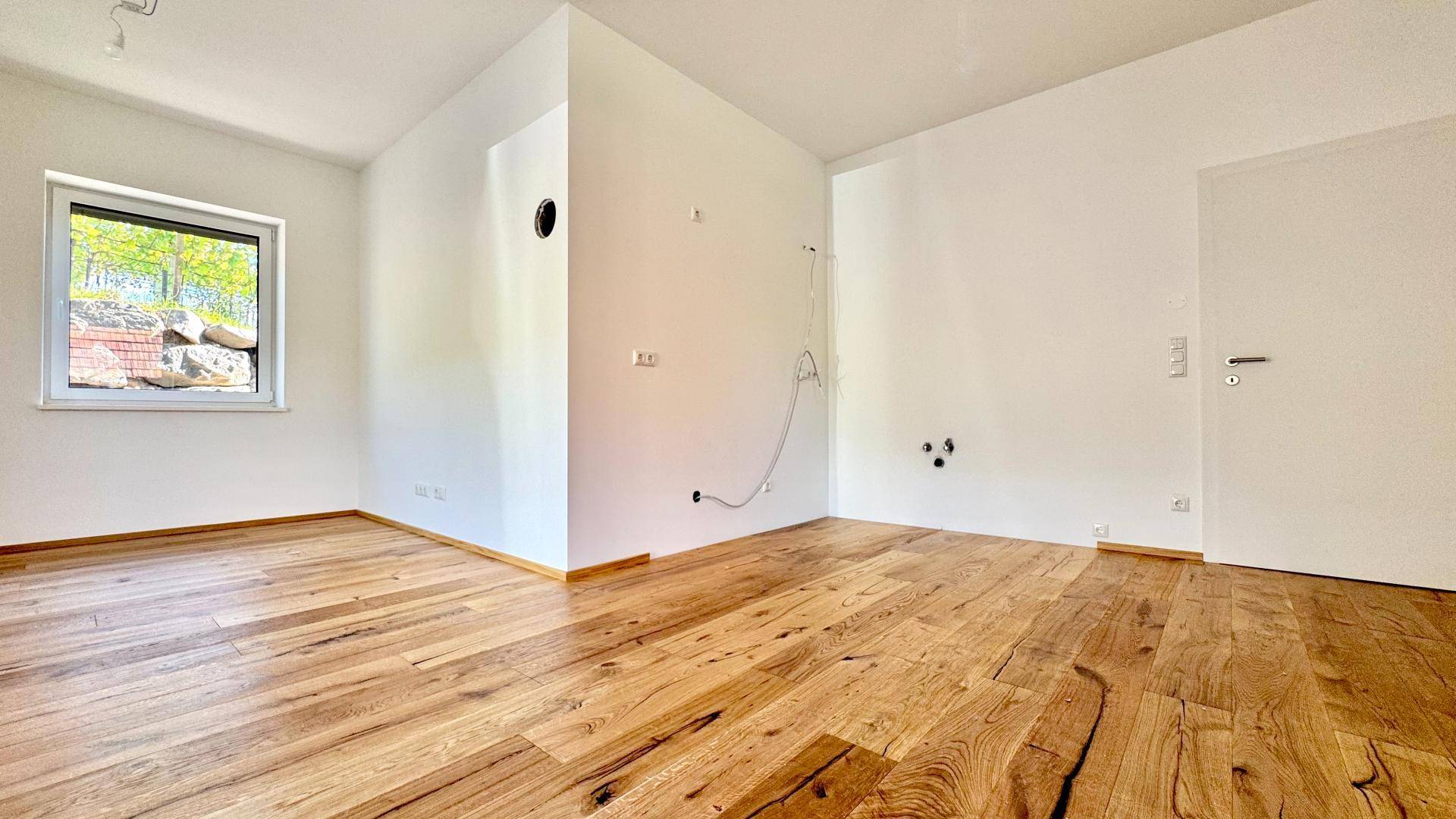 Leerer Raum mit Holzboden, weißen Wänden und vorbereiteten Anschlüssen für eine mögliche Nutzung.