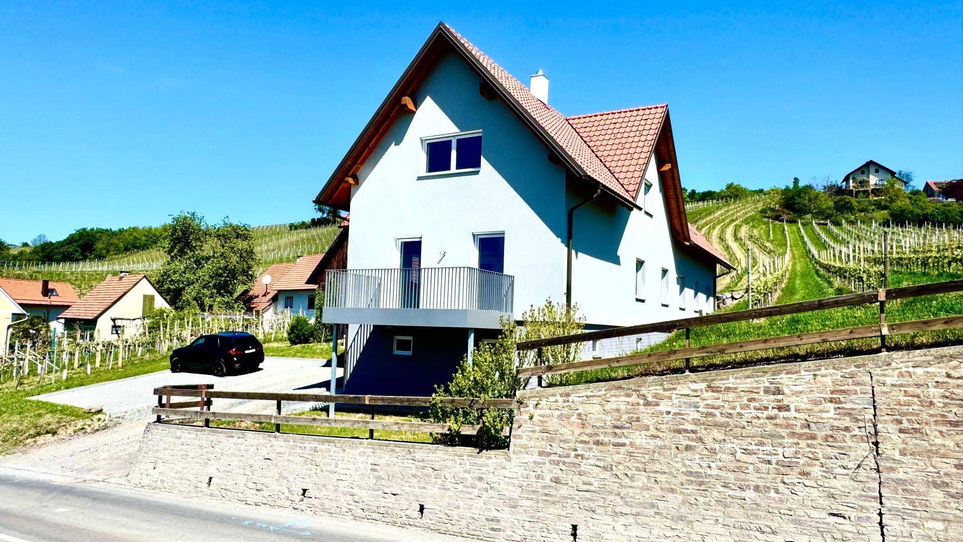 Vorderansicht des Hauses von der Straße aus, mit Balkon und umliegenden Weinbergen.