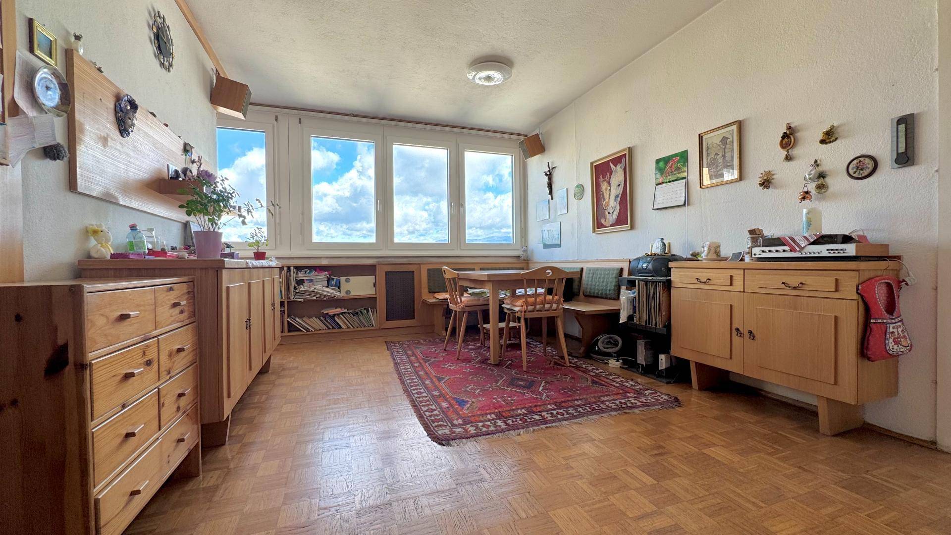 Geräumiger Wohn- und Essbereich mit Parkettboden, Holzmöbeln und weitem Ausblick.
