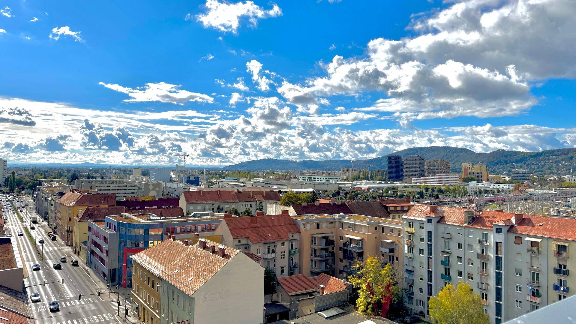 Weitläufiger Blick über die Stadt mit Wohngebäuden, Straßen und Bergen am Horizont.