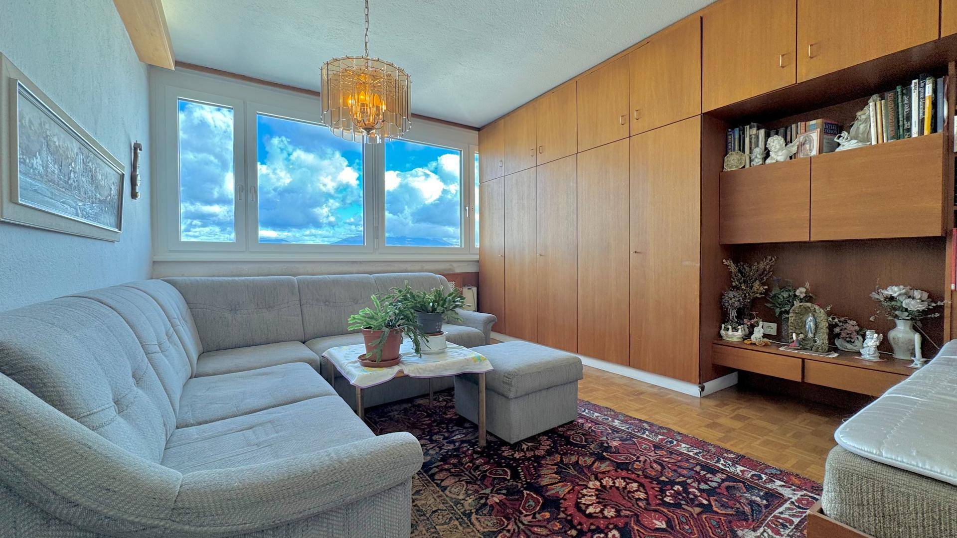 Geräumiges Wohnzimmer mit bequemer Couch, Holz-Einbauschränken und einem dekorativen Kronleuchter.
