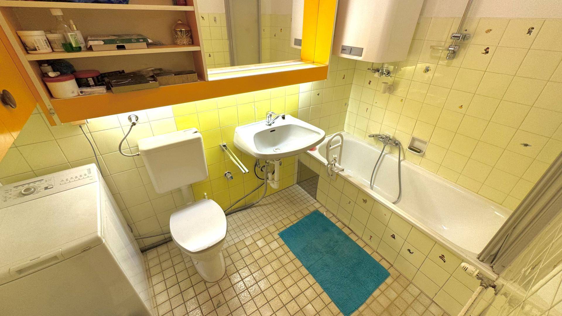Badezimmer mit gelben Fliesen, Badewanne, Toilette, Waschbecken und einer Waschmaschine.