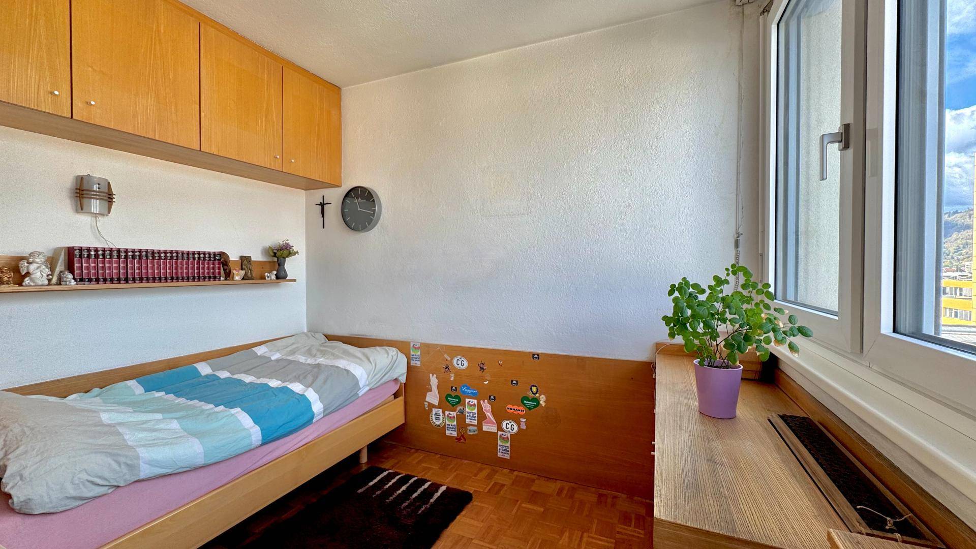 Gemütliches Schlafzimmer mit Einzelbett, Holzmöbeln und einem Fenster, das Tageslicht hereinlässt.